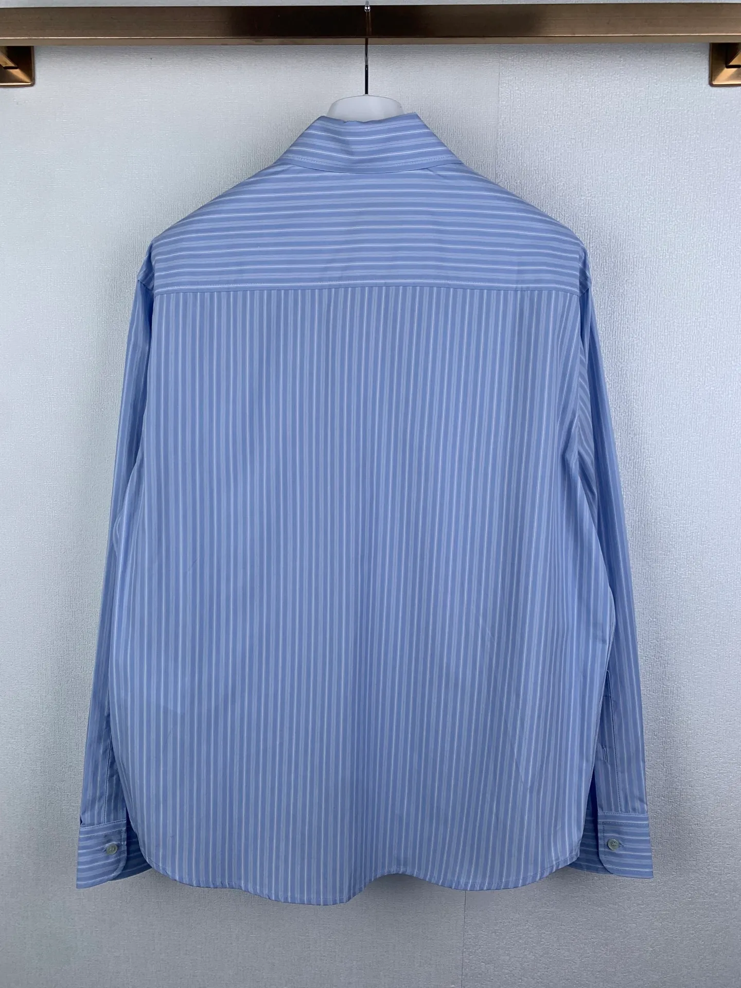 AMI embroidered love heart decorated blue and white striped long-sleeved shirt. Fabric selection: Made of 100% cotton poplin fabric. The pure cotton fiber can quickly absorb moisture and sweat, making it refreshing and not stuffy when worn for a long time. The unique plain weaving process of poplin makes the fabric both soft and skeletal, not easy to wrinkle and deform, and the upper body is neat and clean. Coupled with the fine blue and white stripes all over the body, the light color scheme is gentle and elegant, which can meet the needs of different scenes. Process 1: Accurately mark the embroidery position on the chest patch pocket to ensure that the pattern does not shift and does not destroy the overall beauty of the striped fabric. High-count embroidery threads of the same color as the fabric are selected, and flat stitch embroidery technology is used. The stitches are evenly tracked, the edges are clean and neat, and the love outline is simple and smooth. It retains recognition without irritating the skin. It is blended into the striped texture in a low-key manner to avoid an abrupt feeling, while ensuring that the embroidery threads are Wear-Resistant. 2: After the embroidery is completed, perform high-temperature ironing and thread trimming to ensure that the pattern is smooth and compliant, and it is not easy to lose thread or warp after being worn for a long time. Details: 1. The collar seat adopts double-layer reinforcement technology, which is not easy to collapse and deform after long-term wear. The collar corner has a soft arc, which can modify the neck line without being too sharp, making it neat and decent. 2. The inner side of the placket has hidden hemming treatment to avoid burrs on the fabric, while enhancing structural stability and preventing it from deforming after multiple washes. Accessories: One to one customized buttons Size: S M L XL